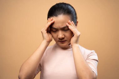 Asyalı kadın hastaydı. Başı ağrıyordu. Bej arka planda tek başına duruyordu..