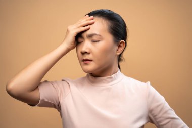 Asyalı kadın hastaydı. Başı ağrıyordu. Bej arka planda tek başına duruyordu..