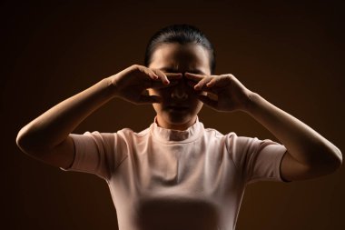 Asyalı kadın gözleri ağrıyordu, gözlerini kaşındırıyordu, bej arka planda tek başına duruyordu. Alçak tuş.