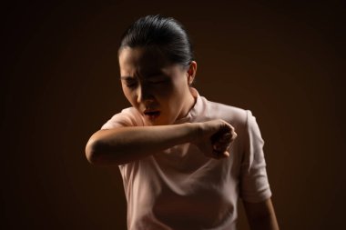 Asyalı kadın boğazı ağrıyordu, öksürüyordu, hapşırıyordu ve bej arka planda tek başına duruyordu. Alçak tuş