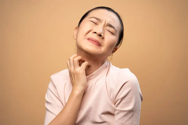 Asian woman was sick with irritate itching her skin, scratching her skin, standing isolated on beige background.