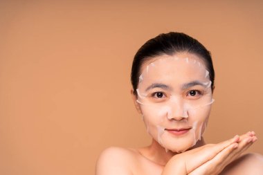 Yüzünde maske olan Asyalı bir kadının bej arka planda duran portresi. Kozmetik Güzellik Spası.