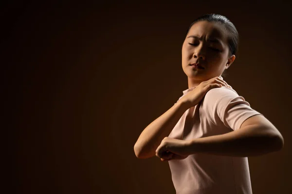 アジア系の女性は体に触れると体の痛みに悩まされ ベージュ色の背景に孤立して立っていた 鍵が低い — ストック写真