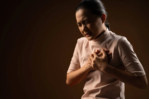 Asian woman was sick with chest pain standing isolated on beige background. Low key