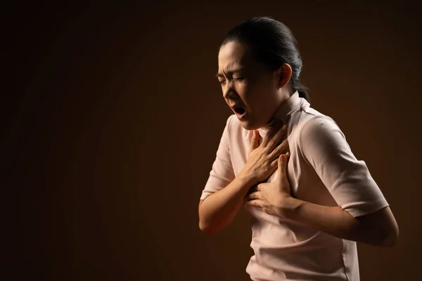 Asian woman was sick with chest pain standing isolated on beige background. Low key
