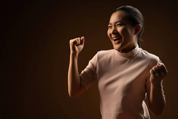 アジアの女性は自信を持って立って彼女の拳を示す幸せベージュの背景に孤立した勝利のジェスチャーを作ります 鍵が低い — ストック写真