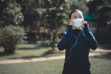 Köyün parkında koşan, müzik dinleyen ve maske takan Asyalı kadının portresi. Koruyucu kirlilik ve koruma virüsü, koronavirüs ve parkta koşmak için maske takan bir kadın..