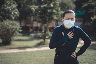 Köyün parkında koşan, müzik dinleyen ve maske takan Asyalı kadının portresi. Koruyucu kirlilik ve koruma virüsü, koronavirüs ve parkta koşmak için maske takan bir kadın..
