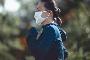Köyün parkında koşan, müzik dinleyen ve maske takan Asyalı kadının portresi. Koruyucu kirlilik ve koruma virüsü, koronavirüs ve parkta koşmak için maske takan bir kadın..