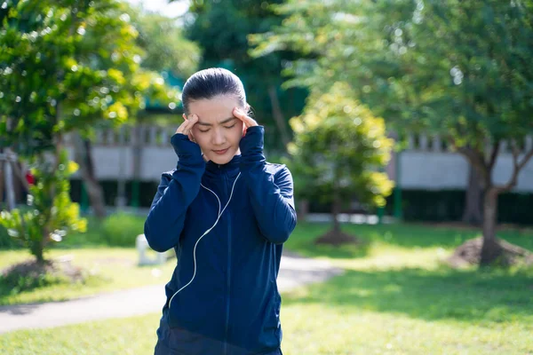 Portrait of Asian woman was sick with headache at park listening to music. Woman exercise at park was sick with headache.