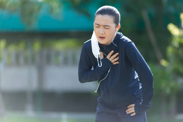 Portrait of Asian woman running at village park listening to music and wearing mask. Woman wearing mask for protective pollution and protection virus, coronavirus and running at park.