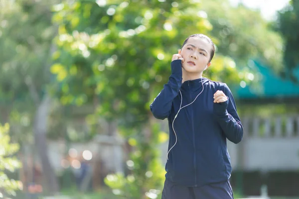 Portrait of Asian woman wearing earphones listening to music was sick with irritate itching her skin at park. Woman exercise at park itching her skin.