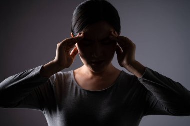 Asyalı kadın hastaydı. Başı ağrıyordu. Arka planda tek başına duruyordu. Alçak tuş.