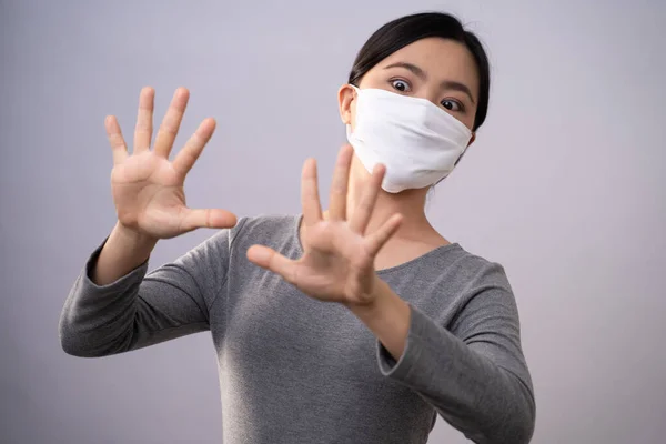 Don\'t Touch Your Face. Asian woman wearing protective face mask showing hand making stop sign standing isolated on background. Prevention Coronavirus COVID-19 concept.