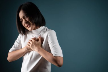 Asyalı kadın göğüs ağrısı nedeniyle hastaydı ve mavi arka planda tek başına duruyordu. Sağlık hizmetleri kavramları.