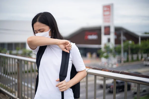 Asian woman wearing protective face mask prevention virus and pollution, coughing and standing at overcrossing city street. New lifestyle with Corona Virus COVID-19.
