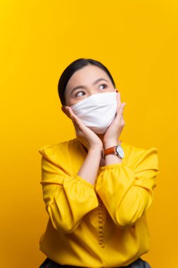 Korunma virüsü için koruyucu yüz maskesi takan Asyalı kadın ve sarı arka planda izole edilmiş hastalık.