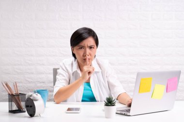 Kadın evde dizüstü bilgisayar kullanarak oturuyor ve sessiz bir jest yapıyor.