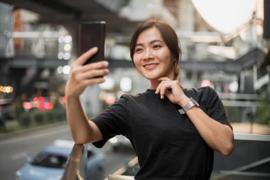 Mutlu Asyalı kadın şehirde selfie çekiyor.