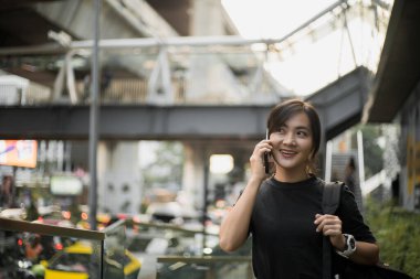 Şehirde akıllı telefonla konuşan mutlu Asyalı kadın.