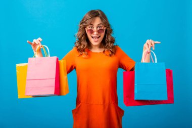 Heyecanlı, gülümseyen stil sahibi bir kadının portresi turuncu modaya uygun elbiseler içinde alışveriş çantalarını mavi arka planda, izole edilmiş, renkli, inanılmaz bir satış, bahar moda trendi