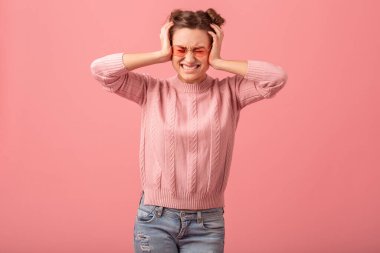 Pembe süveter ve pembe gözlüklerle pembe stüdyo arka planda izole edilmiş, baş ağrısı, stres ve başını tutan genç ve güzel, komik bir kadın.