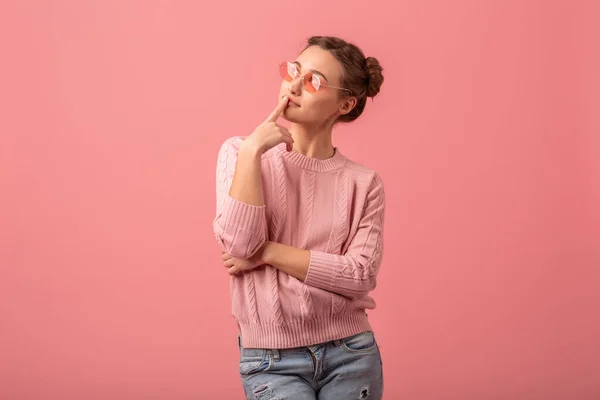 ピンクのセーターとサングラスを着た若い女性がピンクのスタジオの背景に隔離され — ストック写真