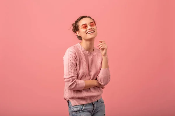 ピンクのセーターとピンクのスタジオの背景に隔離されたサングラスで誠実な笑顔を持つ若い可愛い女性 — ストック写真