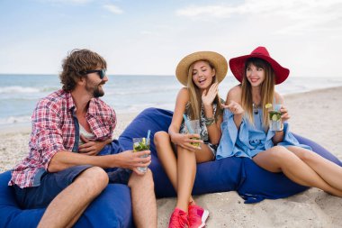 Genç hipster arkadaşları plaj kafede tatil yapıyor, mojito kokteyli içiyor, mutlu pozitif, yaz stili gülümsüyor mutlu iki kadın ve erkek birlikte eğleniyorlar, sohbet ediyorlar, flört ediyorlar, romantizm yaşıyorlar, üç.