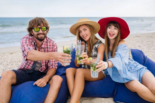 young hipster company of friends on vacation at beach cafe, drinking mojito cocktail, happy positive, summer style, smiling happy, two women and man having fun together, talking, flirt, romance, three