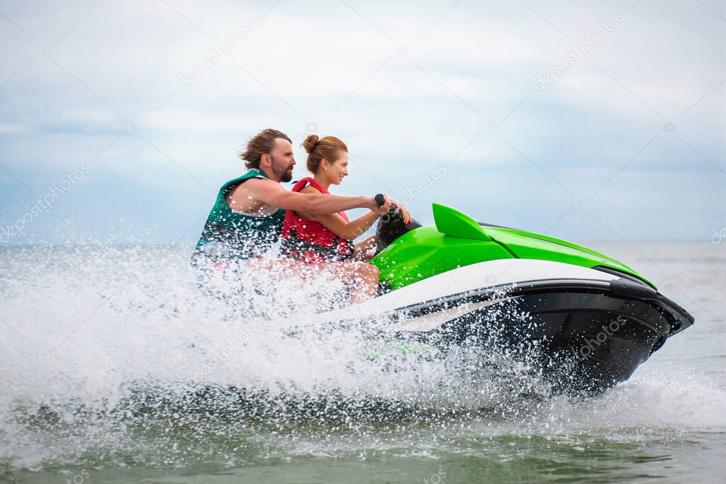 young people having fun driving on high speed on water scooter, man and woman on summer vacation, friends doing active sport