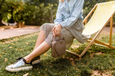 Gümüş ayakkabılar, moda ayakkabıları, güverte sandalyesinde oturan çekici kadın mavi gömlek ve etek, çanta, sokak tarzı aksesuarlar.