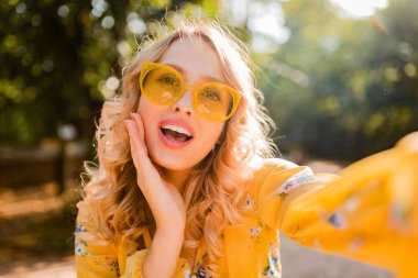 Sarı bluz giyen, güneş gözlüğü takan güzel, şık bir kadının portresi selen fotoğraf, renkli yaz modası, parlak güneşli bir gün, mutlu bir ruh hali.