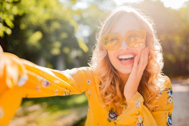 Sarı bluz giyen, güneş gözlüğü takan güzel, şık bir kadının portresi selen fotoğraf, renkli yaz modası, parlak güneşli bir gün, mutlu bir ruh hali.