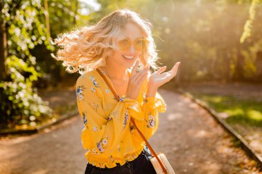 Güzel sarışın, stil sahibi, çığlık atan, sarı bluzlu, güneş gözlüğü takan duygusal kadının portresi. Renkli yaz modası, parlak güneşli gün, pozitif neşeli ruh hali, komik çılgın surat ifadesi.