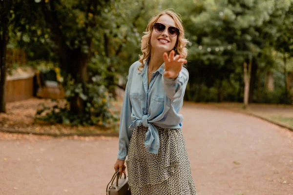 迷人的金发微笑的女人穿着时髦的衣服 蓝色的衬衫和裙子 戴着优雅的太阳镜和钱包 走在公园里 走在大街上时尚的秋风中 心情愉悦 — 图库照片