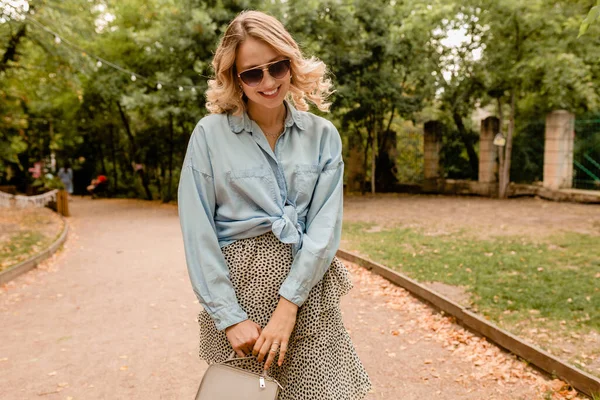 迷人的金发碧眼坦率的女人穿着时髦的蓝色衬衫 戴着优雅的太阳镜和钱包 走在公园里 时尚的街道 秋天的风格 快乐的心情 卷曲的头发 — 图库照片