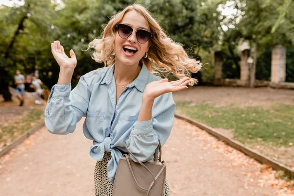 매력적 금발웃는 여자가 선글라스와 지갑을 걸치고 공원을 거리의 스타일 곱슬머리흔들며 — 스톡 사진