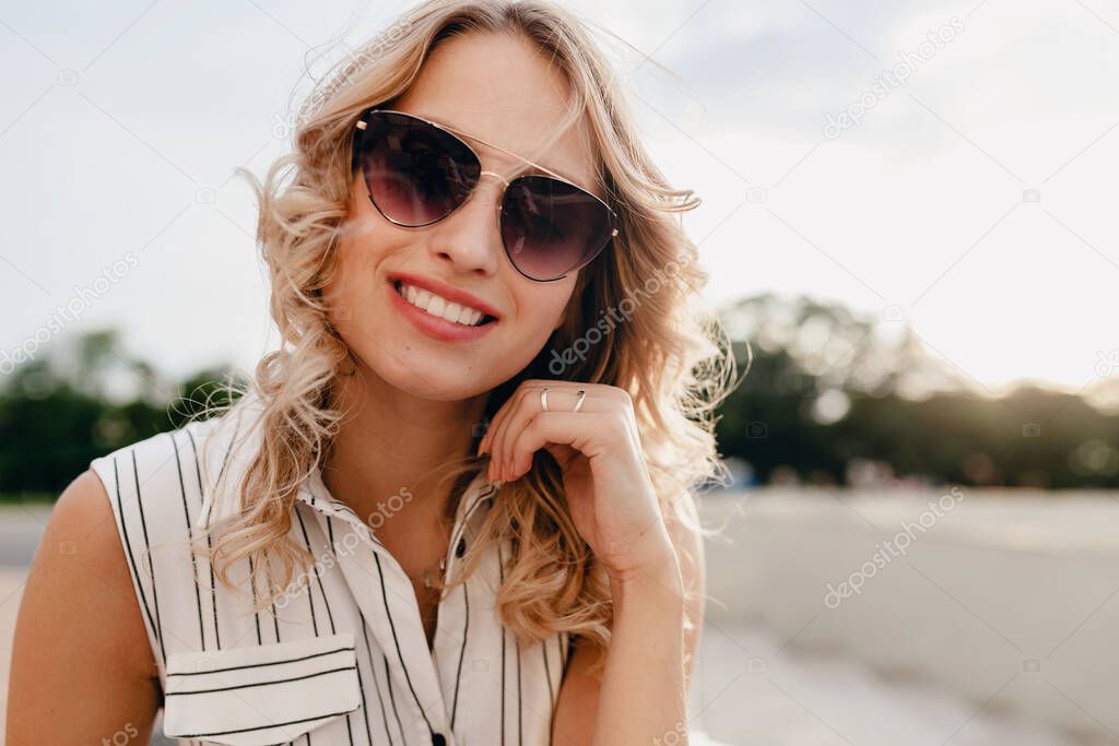 close-up portrait of young attractive stylish blonde woman in city street in summer fashion style dress wearing sunglasses, laughing with candid smile white teeth, sunny