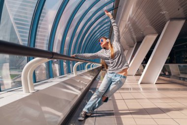 Şehirli modern binada dans eden genç hippi kadın gündelik kıyafetler içinde kulaklıkla müzik dinliyor, tatilde olan öğrenci kot pantolon, süveter ve güneş gözlüğü takıyor.