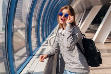 Kentsel modern binalarda sırt çantalı genç hippi kadın günlük kıyafetler giymiş, tatilde olan öğrenci kot pantolon, süveter ve güneş gözlüğü giyiyor.