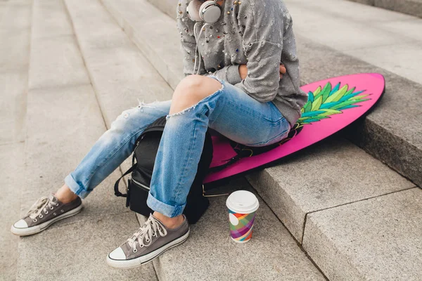 legs in sneakers footwear trend of young hipster woman in street with balance board wearing sweater and jeans, spring summer style, student on vacation, urban trend, headphones