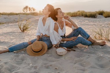 Tropik plajlarda yaz tatilinde şık güzel kadınlar, bohem stili, birlikte arkadaşlar, moda aksesuarları, kot pantolon, hasır şapka, eğlenmek.