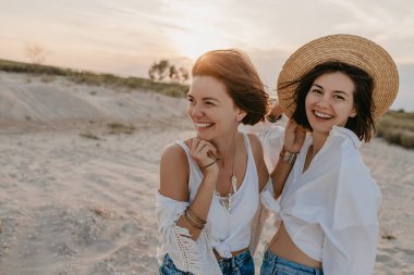 Tropik plajlarda yaz tatilinde şık güzel kadınlar, bohem stili, birlikte arkadaşlar, moda aksesuarları, kot pantolon, hasır şapka, eğlenmek.