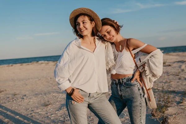 两个年轻女子在日落海滩上玩得很开心 古怪的非二元性别认同 同性恋恋爱 穿着牛仔裤的时髦暑假风格 — 图库照片