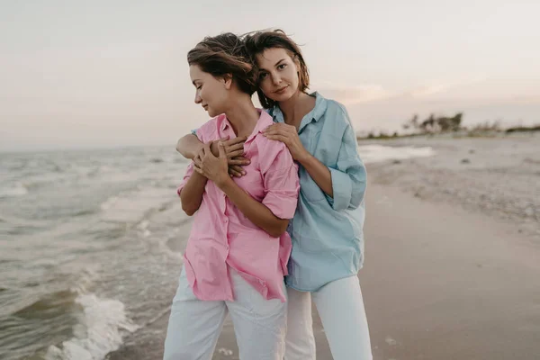 温柔体贴的两个年轻女性朋友在日落海滩上玩得开心 古怪的非二元性别认同 同性恋恋爱 穿着牛仔裤的泡泡暑假风格 — 图库照片