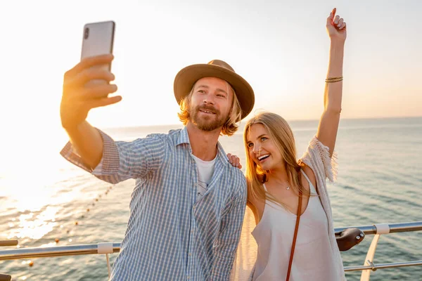 若い魅力的な笑顔の幸せな男と自転車で旅行する女性は 携帯電話のカメラで自撮り写真を撮る 日没時に海でロマンチックなカップル Bohoヒップスタースタイルの衣装 一緒に楽しみを持っている友人 — ストック写真