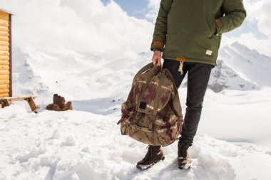 Genç hippi dağlarda yürüyüş yapıyor, kış tatili yapıyor, kuzeye gidiyor, kar, kalın kıyafetler, sırt çantası, kot pantolon, botlar, bacaklar kapalı, detaylar