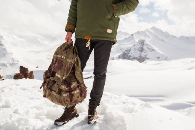 Genç hippi dağlarda yürüyüş yapıyor, kış tatili yapıyor, kuzeye gidiyor, kar, kalın kıyafetler, sırt çantası, kot pantolon, botlar, bacaklar kapalı, detaylar