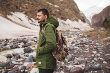 Genç hippi, nehir kenarında yürüyüş, vahşi doğa, kış tatili, seyahat, sırt çantası, sıcak kıyafetler, anorak, dağ manzarası, aktif.